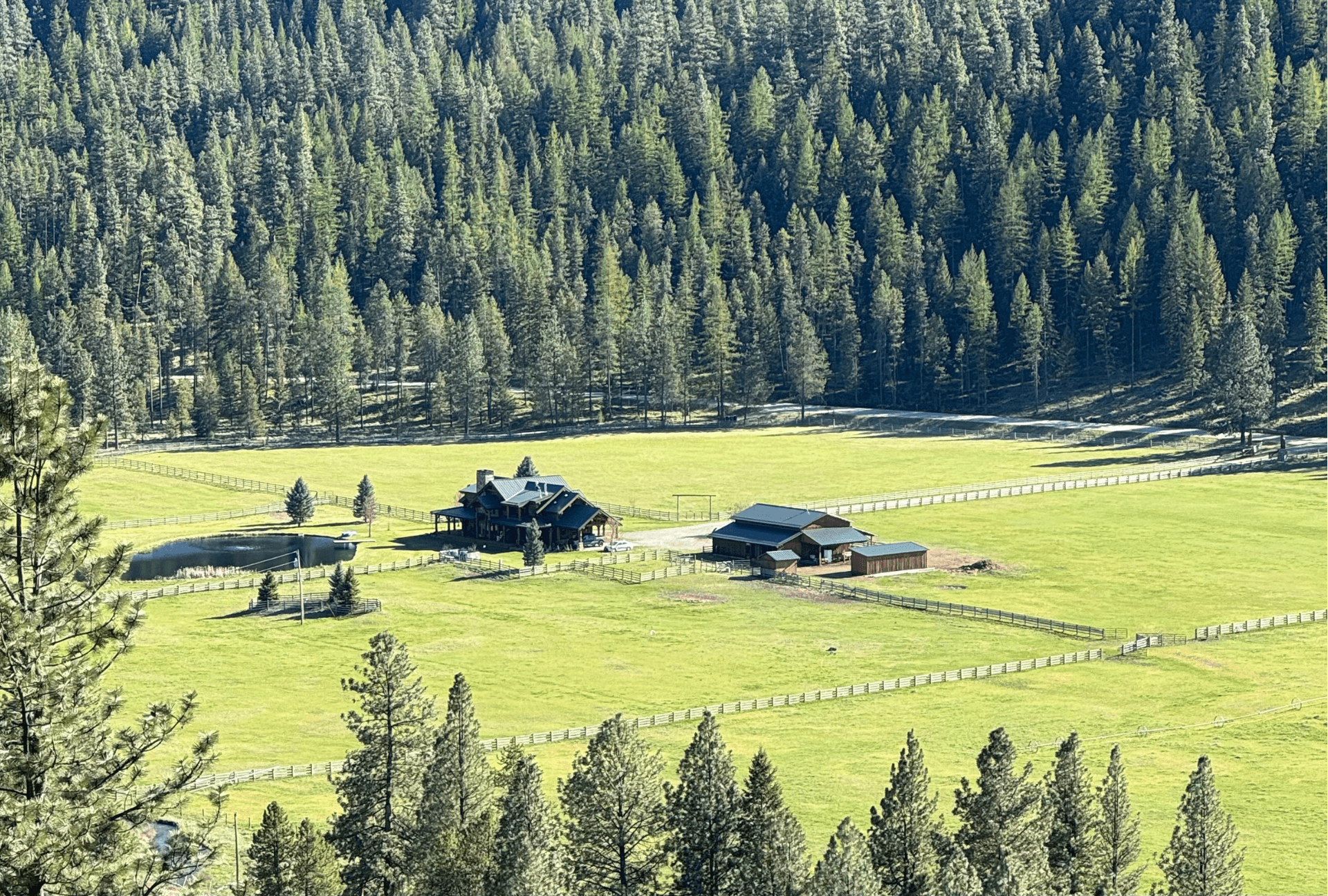 Elevated view of the ranch nestled in green pasture and forest